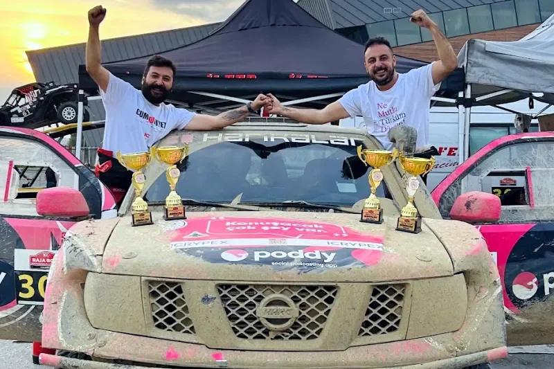 Atilla Baybara and co-pilot Cuneyt Gokturk raising fists over the muddy rally car with four trophies